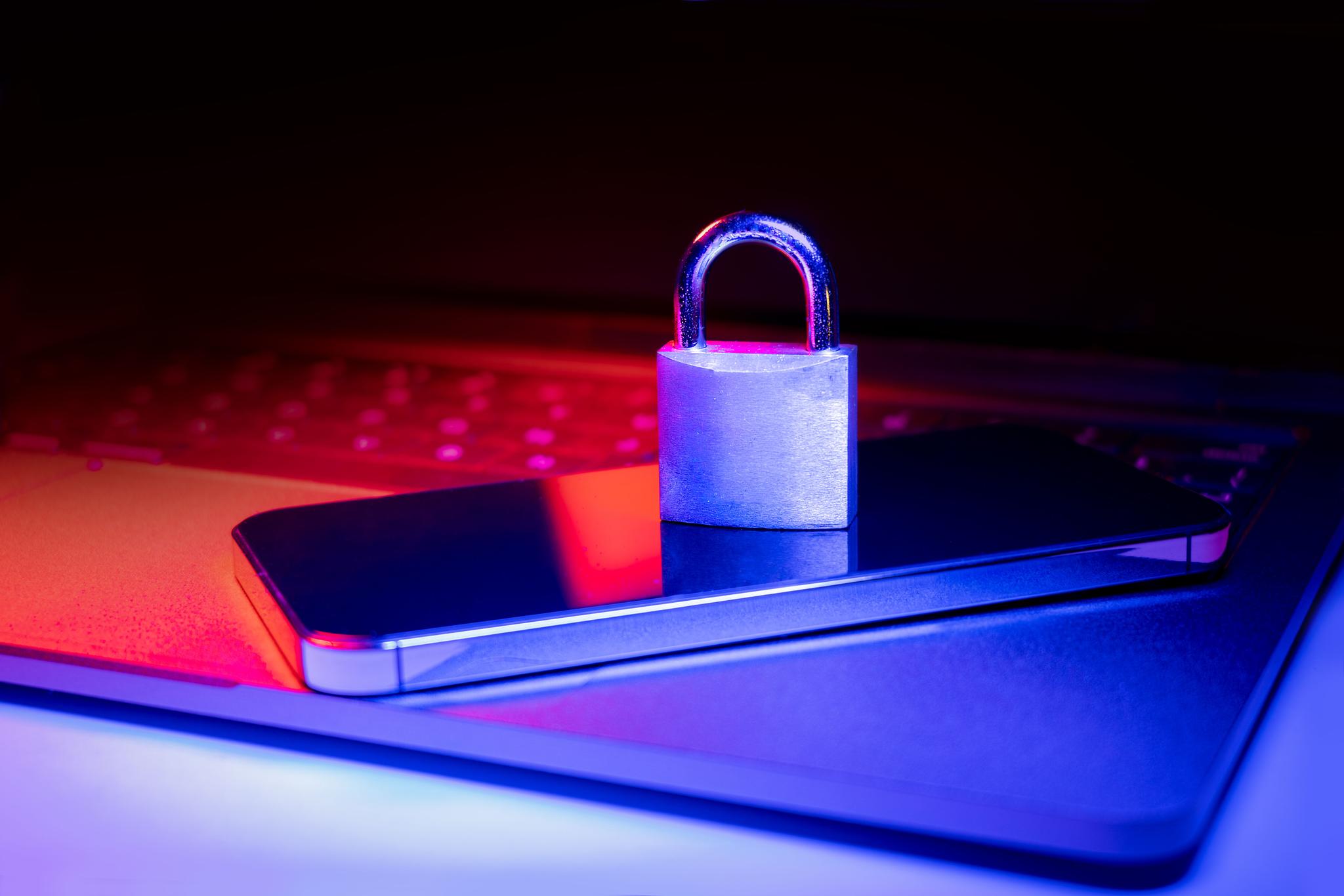 Closeup of a padlock on a laptop and phone illuminated with blue and red light.