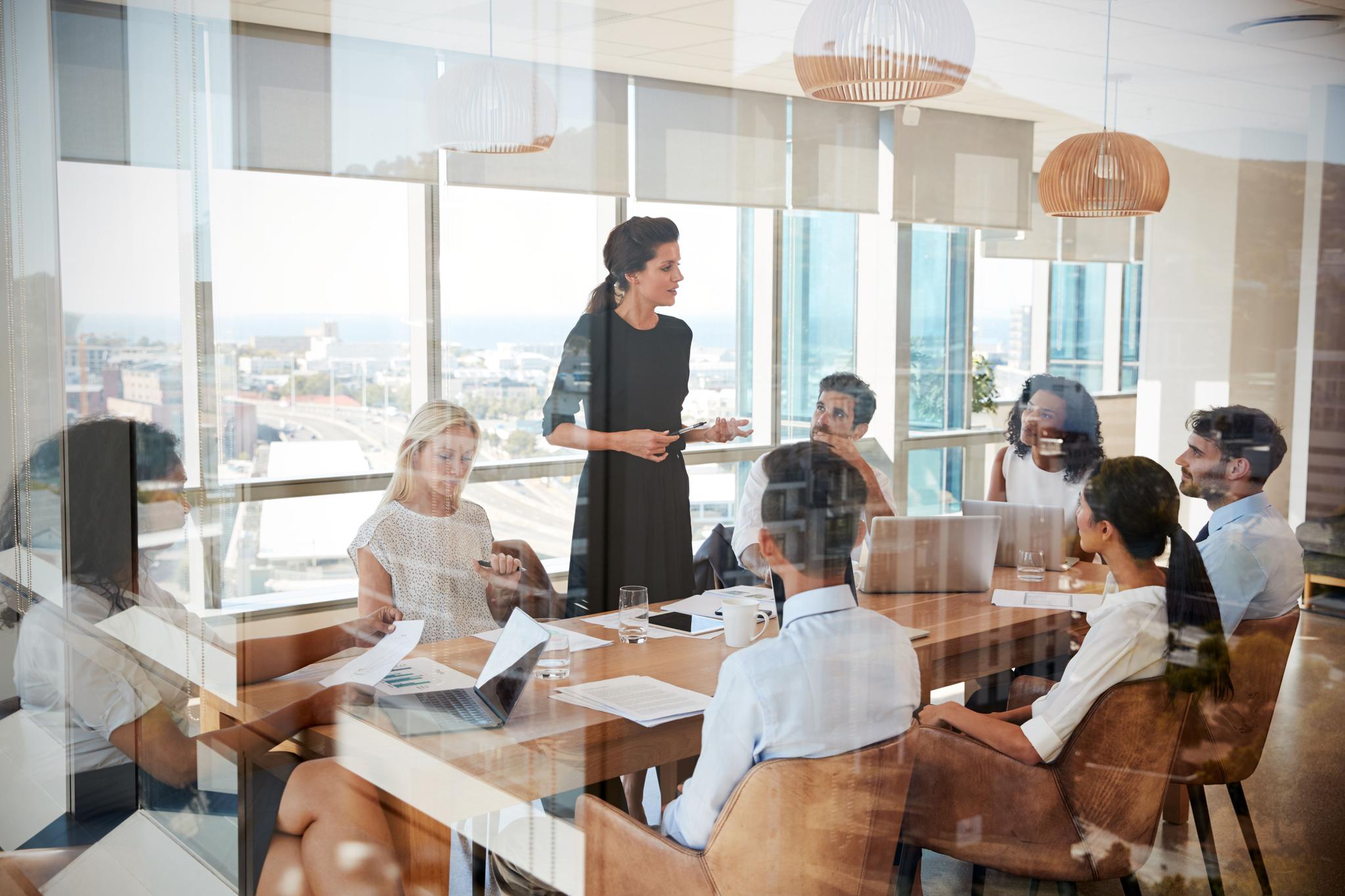 Businesswoman Leads Meeting Around Table Shot Through Door